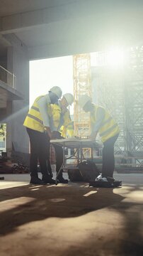 Vertical Screen. Building Construction Site with Workers. High Angle View of Three Architects and Engineers Meeting, Studying Blueprints While Planning Apartment Building Real Estate Development. 