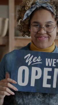 Portrait of African American entrepreneur pottery workshop owner changing Closed to Open sign attracting customers standing indoors in studio