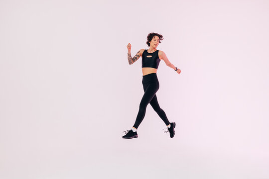 Full length of a young woman in black fitness wear jumping in a studio