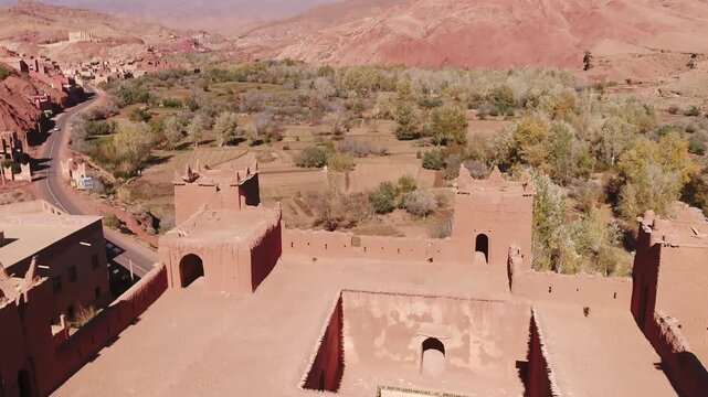 Elevated aerial shot revealing the inner courtyard, rooftop layout, and crenelated towers of a traditional red mudbrick Kasbah in Tinghir, Morocco.