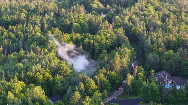 Multiple emergency vehicles on road by forest fire in Rawdon, Quebec, Canada, aerial view.