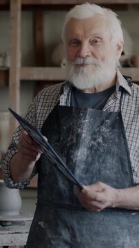 Senior man changing Closed to Open sign standing in workshop reopening pottery studio and welcoming clients. Small business and traditional craft concept.