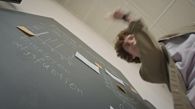 Portrait of Caucasian young adult man dancing enthusiastically, presenting business strategy near chalkboard with sticky notes. Low angle view ideal for startup, workplace or education projects