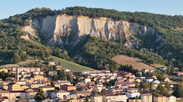 Monte Giogo dominates Lugagnano Val d'Arda with pale Pliocene clay cliffs, wooded slopes and cultivated land in Piacenza, Emilia-Romagna, Italy, drone forward flyover