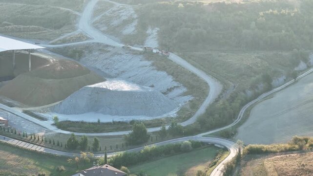 Clay quarry expands across excavated benches and haul roads in Lugagnano Val d'Arda, Piacenza, Emilia-Romagna, Italy, with agricultural land surrounding the site, drone pullback