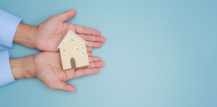 Gentle hands securely hold wooden model expressing peaceful feeling for home ownership protection and financial safeguard vision