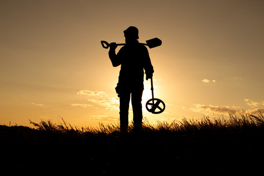 Silhouette of a Man in Panama Hat with Shovel and Detector at Sunrise