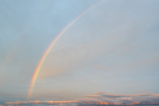 Glowing rainbow arc above soft evening clouds, colorful sky phenomenon
