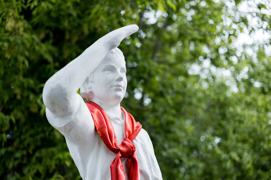 White statue of a pioneer boy saluting with a red neckerchief in a park
