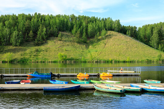 Colorful rowboats moored at a wooden pier on a lake with green hills