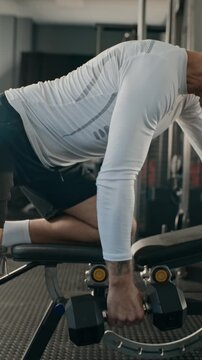 Vertical video of Caucasian middle aged man performing one-arm dumbbell rows on workout bench in gym. Footage fits fitness training apps and social media sports marketing