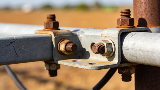 Closeup of rusty bolts and metal brackets holding a sensor in a farm field for smart agriculture