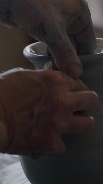 Slow motion of beautiful ceramic vase turning on throwing wheel and male hands potter making earthenware in workshop. Traditional arts and hobby concept.