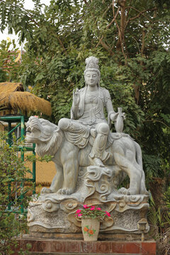 Stone Guanyin statue sitting on sacred lion mount holding ritual water vase, traditional Asian Boddhisattva of compassion sculpture