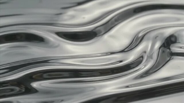 Reflective liquid metal surface forming smooth flowing waves, creating a futuristic abstract background with polished silver textures and fluid motion.