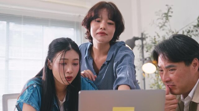Three Asian corporate workers discussing business strategy, pointing at a laptop screen to share information and solve problems together.
