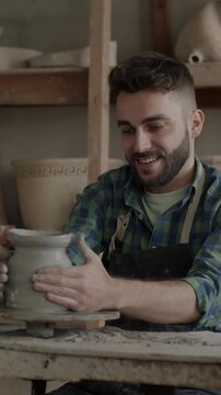 Slow motion of young man in dirty apron using spinning wheel enjoying pottery in workshop. Creative activity and positive emotion concept.