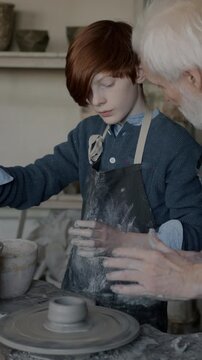 Skilled boy learning pottery with senior teacher enjoying arts education in workshop. Professional occupation and family business concept.