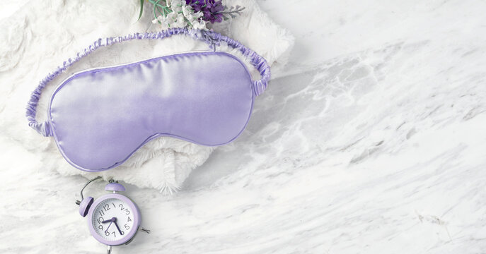 Purple silk eye mask with alarm clock on marble background, good night sleep concept, copy space