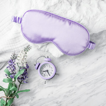 Purple sleep mask on soft fabric with alarm clock and flower on white marble background, Good night sleep concept