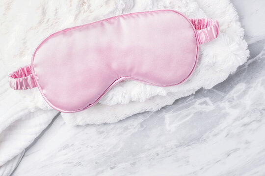 Pink silk sleep mask on soft fabric on white marble background