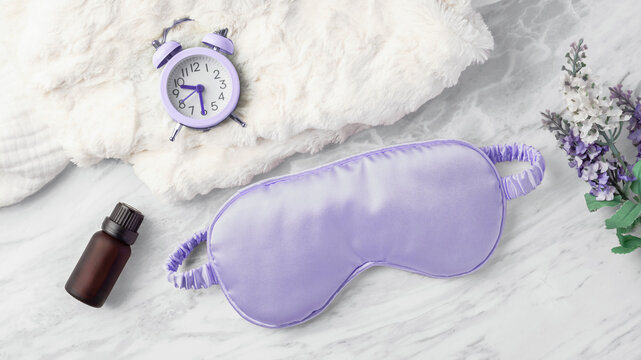 Good night sleep, sleep mask with alarm clock on soft fabric and essential oil bottle on white marble background