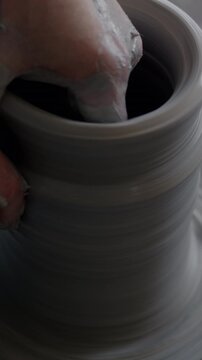 Close-up of skilled potter's hands molding beautiful pot from loam of clay using spinning wheel in studio. Traditional arts and small business concept.