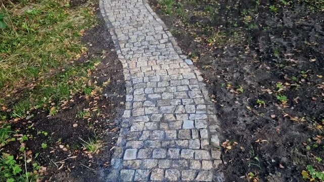 The image shows a narrow path paved with stone setts so-called cat's heads or granite cubes winding through a rural landscape or a park&mdash;such as a ch&acirc;teau park or wooded park.