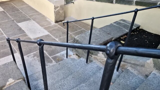 Hand-forged stair railing featuring curved handrail outdoor stone staircase. Black painted steel wrought iron. handrail decorative curved end. Location Outdoor staircase with stone steps and paving wr