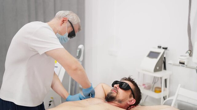 Man undergoing laser hair removal procedure on his chest, with a professional beautician applying a special gel before the epilation treatment in a modern cosmetic clinic