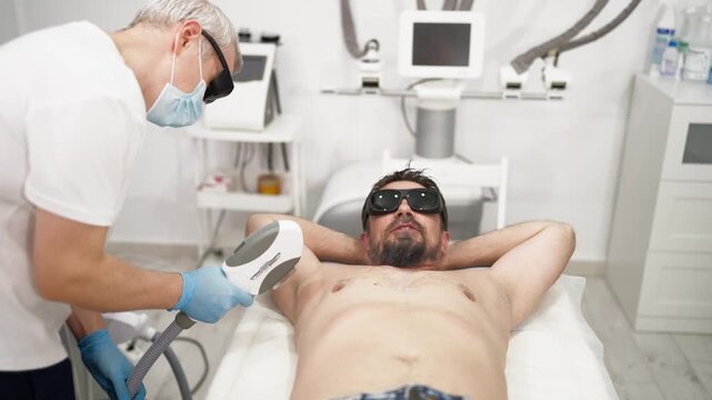 Professional aesthetician performing laser hair removal on male client&rsquo;s underarm in modern beauty clinic, illustrating smooth skin, unwanted hair removal and professional body care treatment