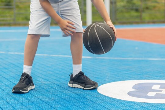 Child practicing basketball with ball on outdoor court