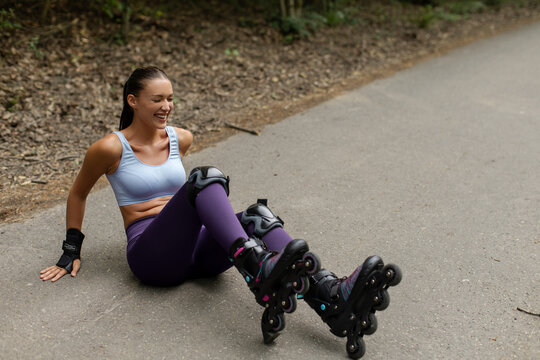 Laughing young woman sitting on the ground after falling while rollerblading