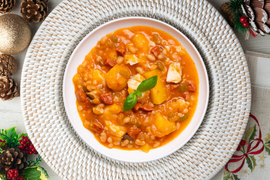 A close-up overhead view of a delicious cod and chorizo stew, garnished with basil, presented with Christmas ornaments