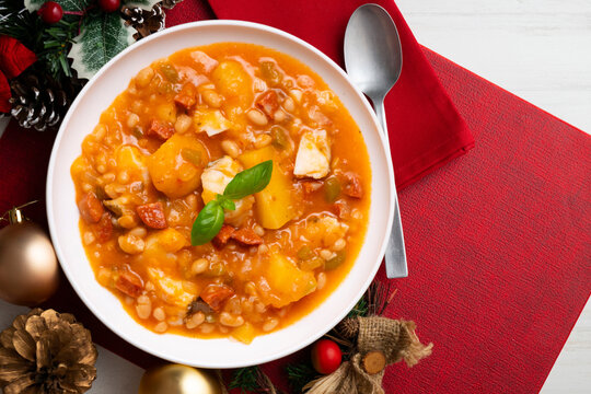 A close-up overhead view of a delicious cod and chorizo stew, garnished with basil, presented with Christmas ornaments
