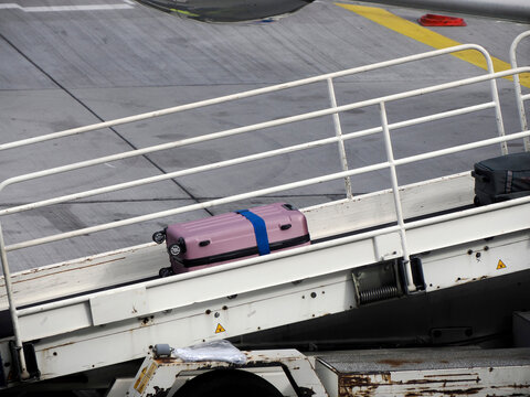 Luggage being loaded into an aircraft cargo hold via a conveyor belt on the airport tarmac