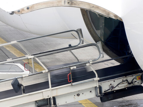 Luggage being loaded into an aircraft cargo hold via a conveyor belt on the airport tarmac