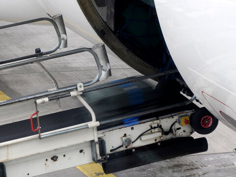Luggage being loaded into an aircraft cargo hold via a conveyor belt on the airport tarmac