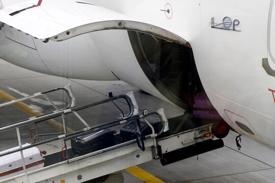 Luggage being loaded into an aircraft cargo hold via a conveyor belt on the airport tarmac