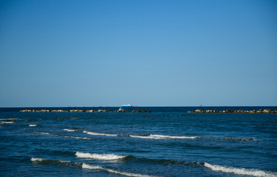 Waves rolling on the shore under a clear blue sky with distant land on the horizon