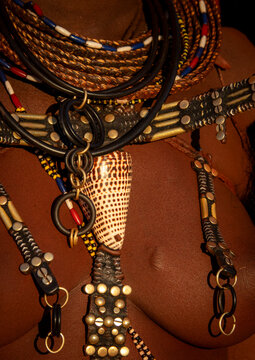Macro view of a cowrie shell pendant hanging among beaded necklaces and brass-studded leather straps, Cunene Province, Oncocua, Angola