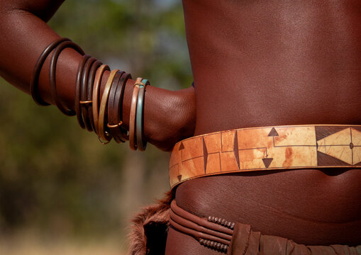 Close-up of a woman's arm stacked with bangles resting near a carved waist belt, Cunene Province, Oncocua, Angola