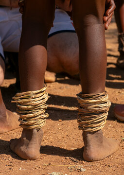 Close-up of two people's legs wrapped in stacked fiber rings above bare feet on red dirt, Cunene Province, Oncocua, Angola