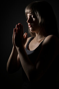 Young woman praying with hands clasped in profile view against a dark background