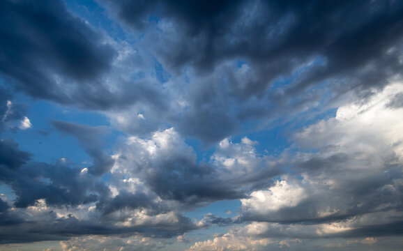 Dramatic blue sky background with dark storm clouds and bright sunlight breaking through white cumulus formations