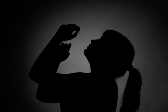Silhouette portrait of a young teenage girl posing against a dark background
