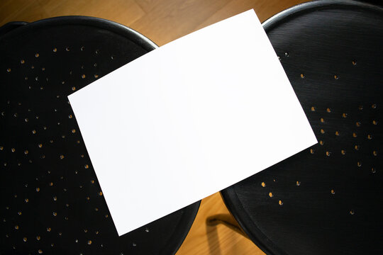 A mockup of a white sheet of A4 paper on black wooden chairs with perforations. Soft, diffused focus. A blank poster with space for text, design, and presentation