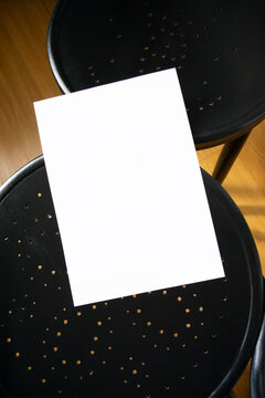 A mockup of a white sheet of A4 paper on a black wooden chair with perforations. Soft, diffused focus. A blank poster with space for text, design, and presentation