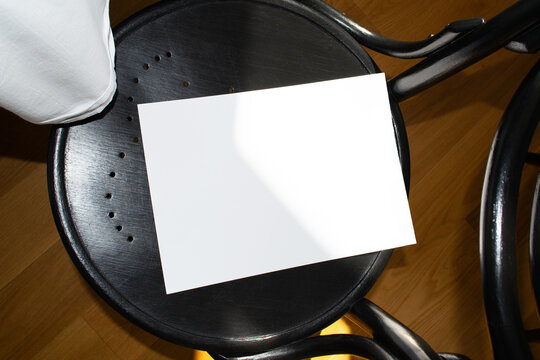 A mockup of a white sheet of A4 paper on a black wooden chair with perforations. Soft, diffused focus. A blank poster with space for text, design, and presentation