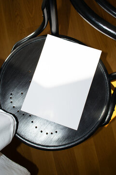 A mockup of a white sheet of A4 paper on a black wooden chair with perforations. Soft, diffused focus. A blank poster with space for text, design, and presentation